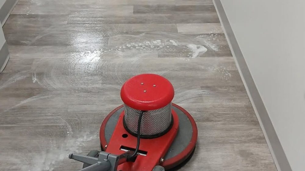 Zimick Bros. red rotary floor buffer working cleaning solution into a commercial LVT vinyl plank floor in an office building