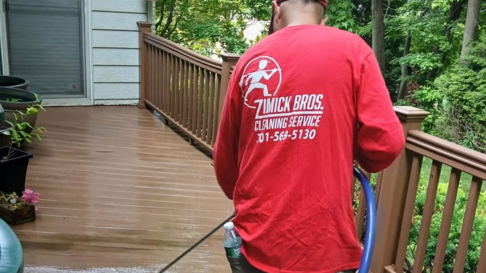 Zimick Bros. cleaning crew member in a red company shirt pressure-washing a stained wood residential deck at a Bergen County, NJ home